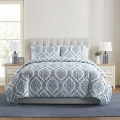 a blue and white bed in a bedroom next to a window with two lamps on either side