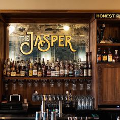 a bar with liquor bottles and glasses on the shelves behind it is an advertisement for the jasper