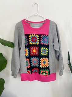 a colorful sweater hanging on a white wall next to a potted plant with green leaves