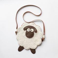 a white sheep purse with brown straps on a white surface, the bag is shaped like an animal's head