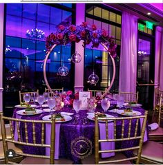 the table is set up with purple flowers and place settings for an elegant dinner party