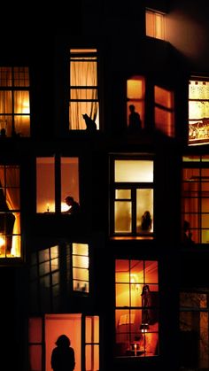 several windows lit up at night with people in the window sill and onlookers