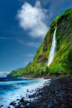 a large waterfall is on the side of a cliff near the ocean with rocks and green vegetation