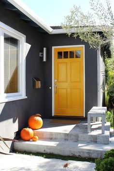 two pumpkins are sitting on the steps in front of a house with yellow doors