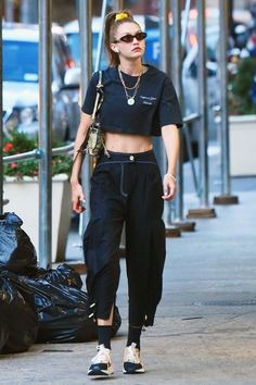 a woman walking down the street wearing black pants and a crop top with her hair pulled back