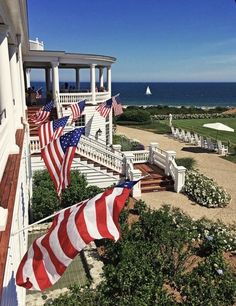 an american flag is hanging on the side of a white house by the beach and ocean