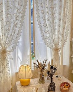 a table topped with vases filled with flowers next to two windows covered in white lace