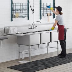 a woman cleaning a kitchen sink in front of two sinks with sprayers on the faucets