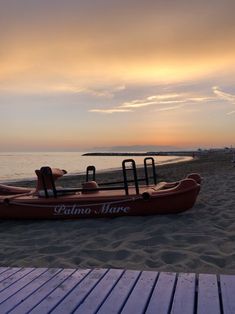 a red boat sitting on top of a sandy beach next to the ocean at sunset