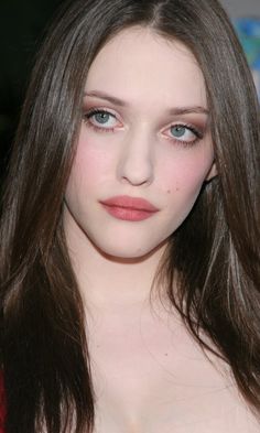 a woman with long brown hair and blue eyes wearing a red dress is looking at the camera