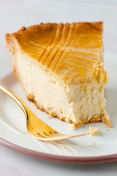 a piece of cheesecake on a white plate with a gold fork next to it