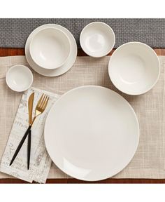 a place setting with white dishes and gold utensils on a linen place mat