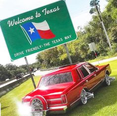 a red car parked under a welcome to texas sign