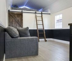 a living room with white walls and wood flooring next to a ladder that leads up to a loft bed