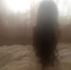 the back of a woman's head sitting on a bed in front of a window