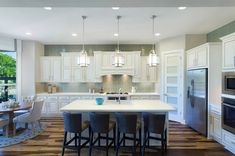 a large kitchen with white cabinets and an island in the middle, surrounded by chairs