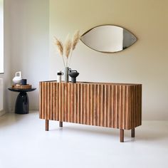 a wooden cabinet sitting in the middle of a room next to a mirror and vase