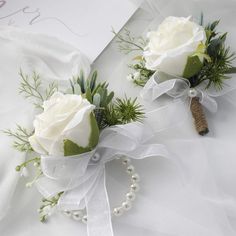 two boutonnieres with white roses and greenery tied to them on a bed