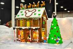 a gingerbread house with mickey mouse decorations on it and a christmas tree in the foreground