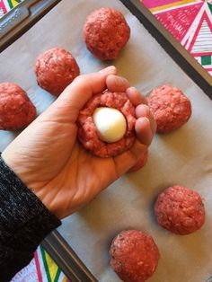 a person is holding an egg in the middle of some meatballs on a baking sheet