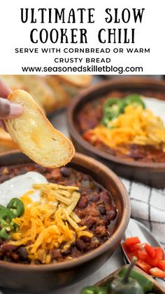 a person is dipping some bread into a bowl of chili and cheese with sour cream on top