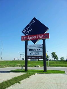 a sign for a designer outlet in the middle of a road with grass on both sides