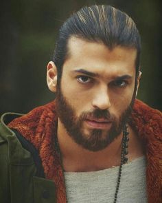 a man with long hair and a beard wearing a necklace is looking at the camera