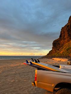 surfboards are sitting on the back of a pick up truck at the beach as the sun sets