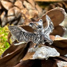 a silver ring with a bat on it sitting on top of a pine cone in the grass