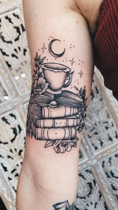 a person with a tattoo on their arm holding a stack of books and a cup