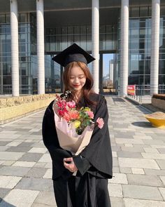 a young woman in graduation gown holding flowers