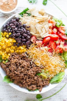 a white bowl filled with taco salad next to tortilla chips and guacamole