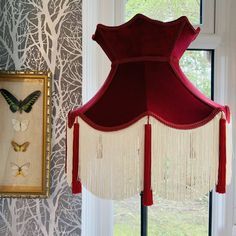 a red lamp shade hanging from the side of a window next to a butterfly painting