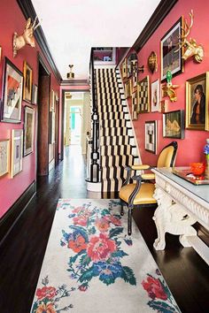 a hallway with red walls and pictures on the wall next to a white table topped with a rug