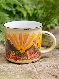 a coffee mug with flowers painted on it sitting on a rock next to some plants