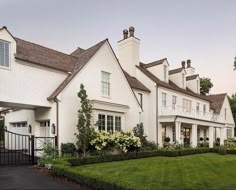 a large white house with lots of flowers in the front yard and bushes around it