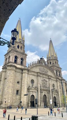 people are walking around in front of an old building with two spires on top