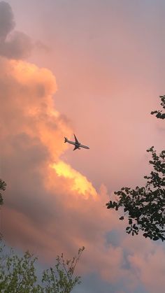 an airplane is flying in the sky at sunset with clouds and trees around it,