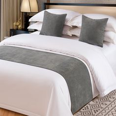 a bed with white sheets and gray pillows