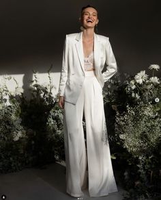 a woman standing in front of flowers and greenery wearing a white suit with wide legs