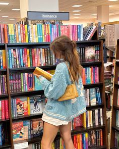 a woman is standing in front of a bookshelf and looking at her book