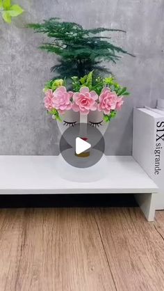 a white shelf with pink flowers on it and a plant in the corner next to it