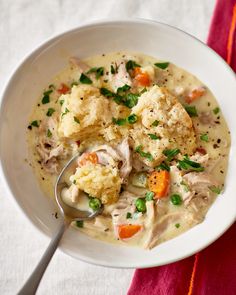 a white bowl filled with chicken and dumplings on top of a red cloth next to a spoon