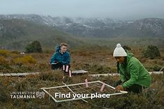 two people in the middle of an open field with mountains in the background and one person holding a pink toothbrush