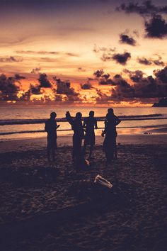 four people standing on the beach at sunset