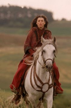 a woman riding on the back of a white horse in a field with tall grass