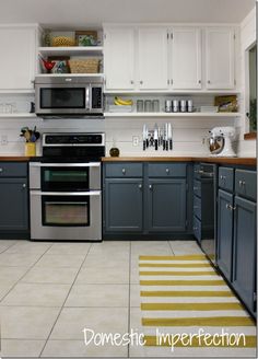 a kitchen with gray cabinets and white walls, yellow rugs on the floor in front of the stove