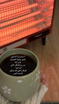 a person holding a cup of coffee in front of an electric heater with arabic writing on it