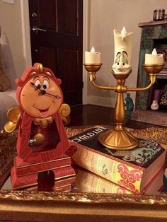 the beauty and the beast figurine is sitting on top of books in front of a candle holder