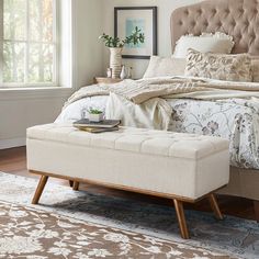 a bed with a tufted upholstered headboard and footstool in a bedroom